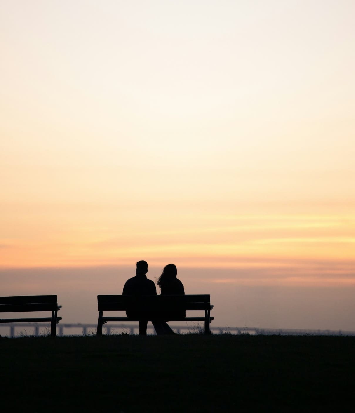 A couple sitting on a bench during sunset